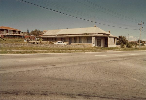 An image of a large house with a verandah with cars in front of it.