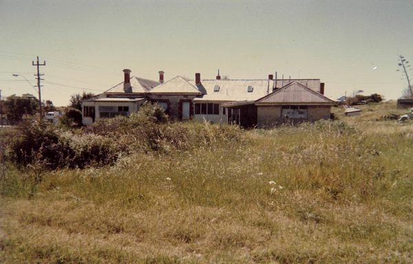 A colour image showing a large house with a corrugated room with overgrown grass in front.